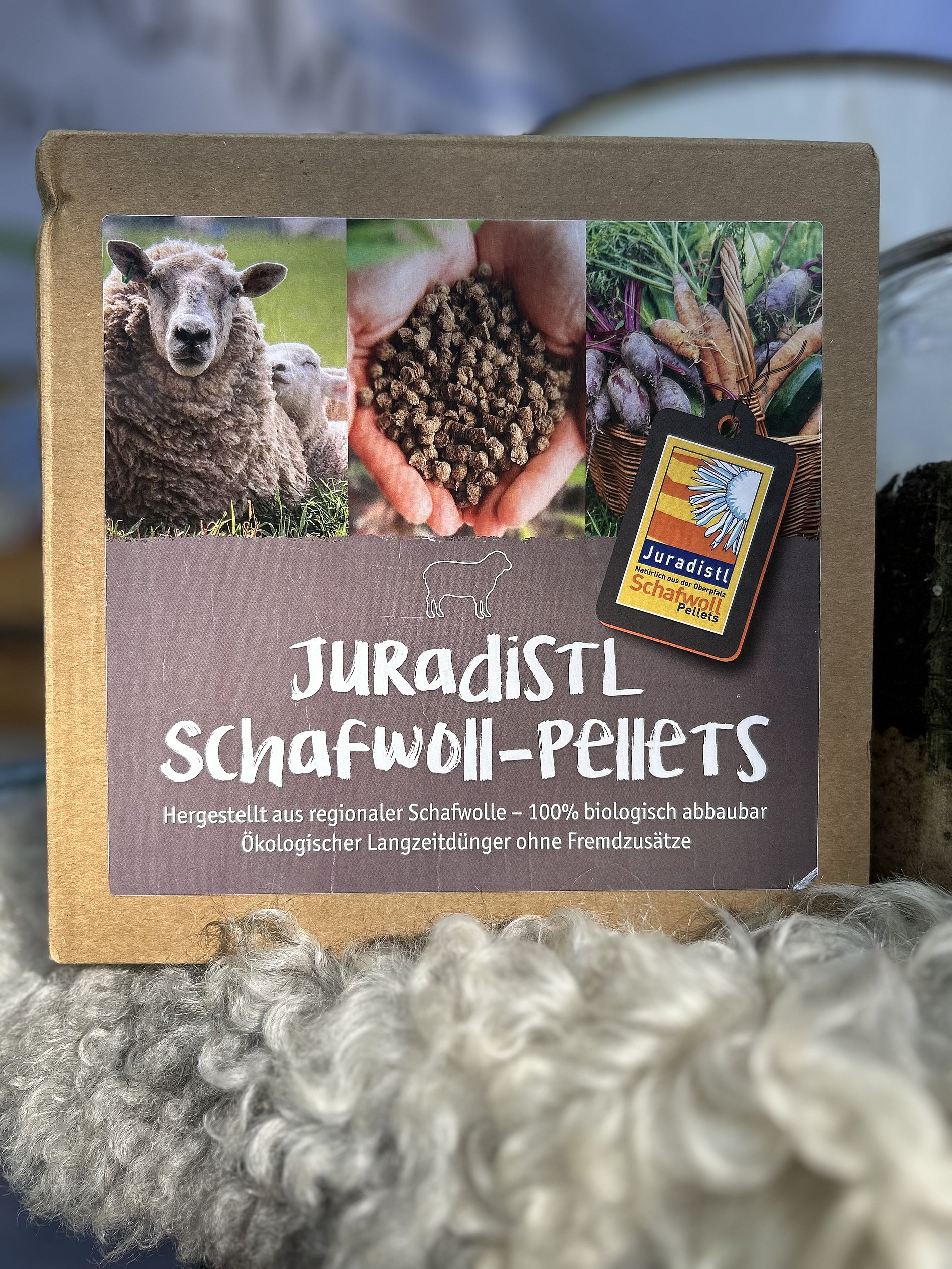 ein würfelartiger Karton mit aufgedrucktem Etikett "Juradistl Schafwoll-Pellets", Menge ist 1 kg